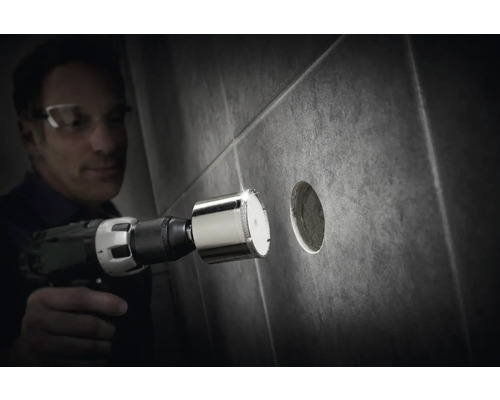 Un homme perce un trou dans un carreau avec une scie cloche diamantée.