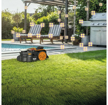 Ein Rasenmähroboter steht auf einem Rasen neben einem Swimmingpool und Gartenmöbeln.