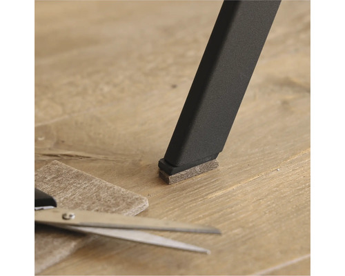 Patins en feutre sur un pied de chaise avec des ciseaux et un morceau de feutre sur le sol