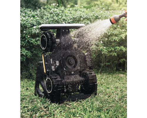 Robot de jardin arrosé avec entraînement à chenilles en utilisation sur une pelouse.
