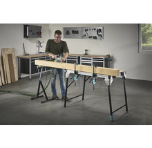 Un homme fraise du bois sur un établi avec des serre-joints dans un atelier