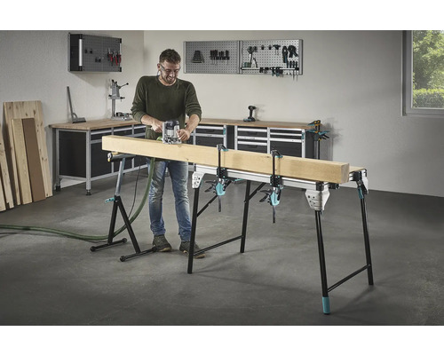 Un homme fraise du bois sur un établi avec des serre-joints dans un atelier