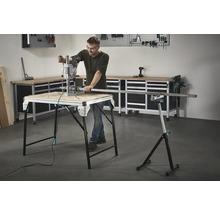 Un homme travaille avec une perceuse sur un établi, avec des outils et un établi en arrière-plan.