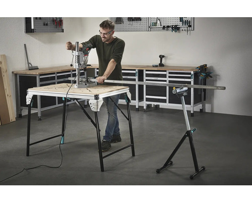 Un homme travaille avec une perceuse sur un établi, avec des outils et un établi en arrière-plan.