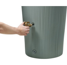 Main installant un robinet en laiton sur un récupérateur d'eau de pluie gris et cannelé.