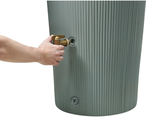 Main installant un robinet en laiton sur un récupérateur d'eau de pluie gris et cannelé.