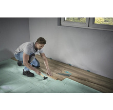 Un homme pose du stratifié avec un marteau et une cale de frappe sur une isolation phonique dans une pièce.