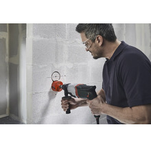 Un homme perce un trou dans un mur avec une scie cloche.