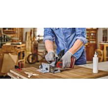 Un homme utilise une fraise à rainurer pour travailler une pièce. Des plaquettes de bois et un flacon de colle sont posés sur la table.