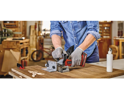 Un homme utilise une fraise à rainurer pour travailler une pièce. Des plaquettes de bois et un flacon de colle sont posés sur la table.