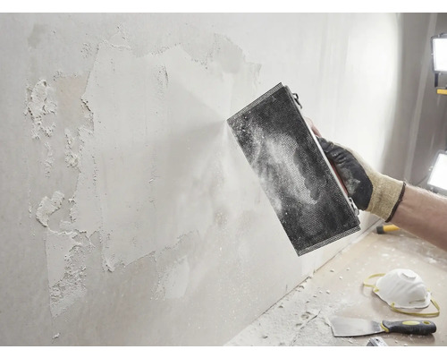 Artisan ponçant un mur avec un outil de ponçage. Projet de bricolage pour la rénovation des murs.