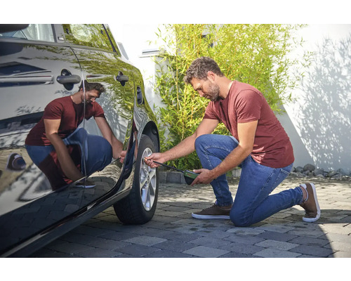 Ein Mann prüft den Reifendruck eines Autos mit einem Reifendruckprüfer.