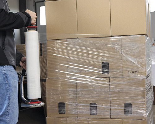 Une personne emballe des cartons avec un dévidoir de film étirable.