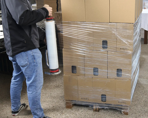 Eine Person verpackt Kartons mit einem Folienwickler auf einer Palette.