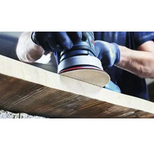 Une personne ponce une planche de bois avec une ponceuse excentrique.