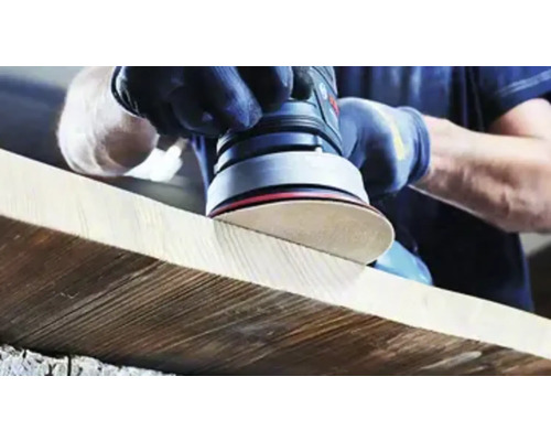 Une personne ponce une planche de bois avec une ponceuse excentrique.