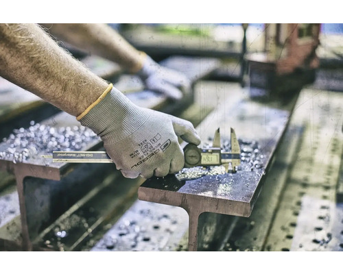 Eine Person misst ein Metallstück mit einem digitalen Messschieber auf einem Träger.