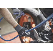 Une personne tenant un tuyau bleu avec une paire de gants de travail nettoie une moto.