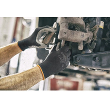 Des mains de mécanicien travaillent sur une roue de voiture avec des gants de protection.
