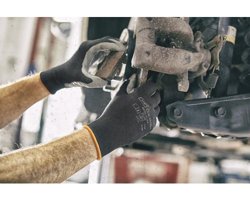 Des mains de mécanicien travaillent sur une roue de voiture avec des gants de protection.