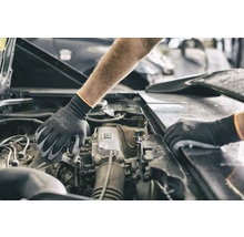 Une personne portant des gants de protection travaille sur un moteur de voiture.