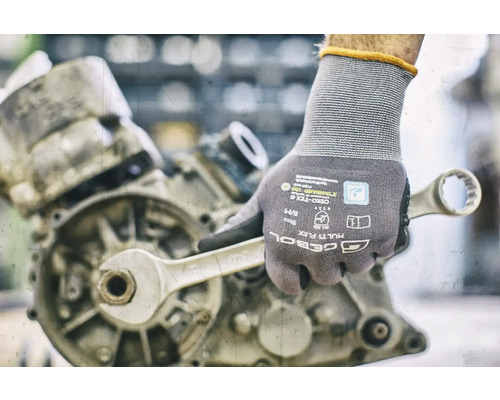 Hand mit Arbeitshandschuh und Schraubenschlüssel an einem Motor