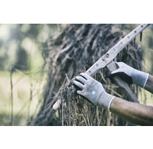 Person mit Handschuhen, die trockenes Gras mit einem hölzernen Rechen aufnimmt