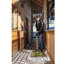 Mann kehrt Schnee mit einem Besen vor einem Holzhaus