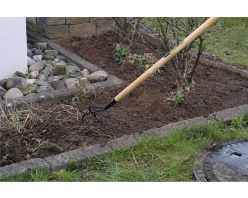 Gartenszene mit einem Sauzahn mit Holzgriff bei der Bodenbearbeitung