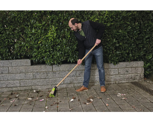Eine Person kehrt Blätter mit einem Strassenbesen.