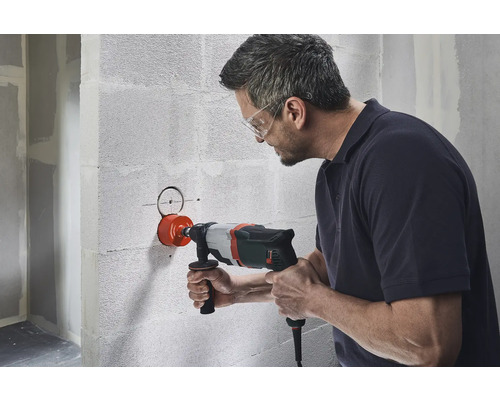 Mann bohrt mit einer Kernbohrmaschine ein Loch in eine Betonwand.