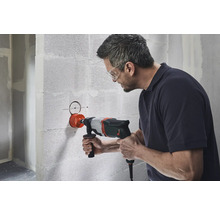 Mann bohrt mit einer Mauerkrone ein Loch in eine Wand.