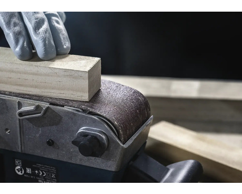 Gros plan d'une ponceuse à bande ponçant une pièce de bois, manipulée par une personne gantée.