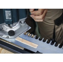 Eine Oberfräse beim Bearbeiten eines Werkstücks mit einer Schablone für Zinkenverbindungen.