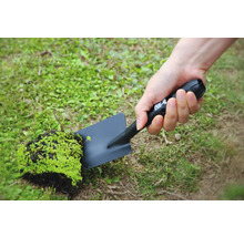 Une personne tient une pelle de jardin noire avec un morceau de terre et des plantes.