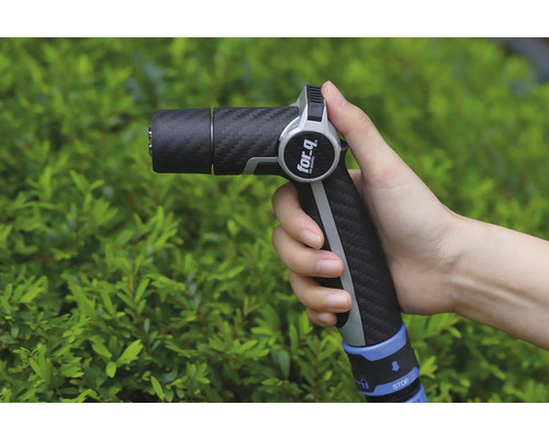 Eine Hand hält eine Gartenspritze der Marke For Q vor einem grünen Busch