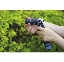 Eine Person hält eine Gartenspritze der Marke for_q vor einem grünen Busch.