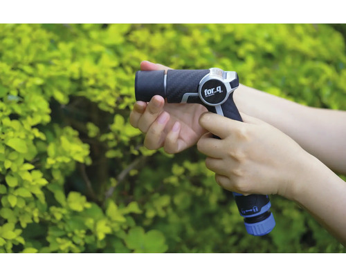 Eine Person hält eine Gartenspritze der Marke for_q vor einem grünen Busch.