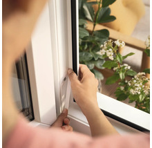 Une personne installe un joint de fenêtre sur un cadre de fenêtre blanc.