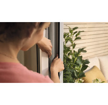 Femme fixant une moustiquaire sur une fenêtre.