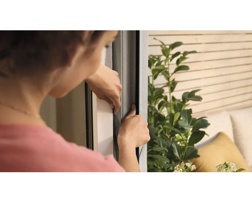 Femme fixant une moustiquaire sur une fenêtre.