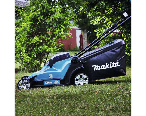 Tondeuse à gazon sans fil Makita avec largeur de coupe de 430 millimètres et bac de ramassage en action sur une pelouse dans un jardin.
