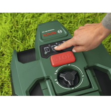 Gros plan d'un robot tondeuse Bosch avec une main touchant le panneau de commande, avec un bouton d'arrêt rouge et un bouton rotatif noir pour régler la hauteur de coupe.