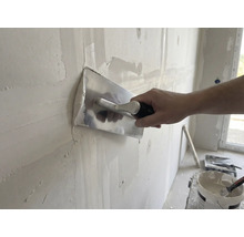 Artisan lisse un mur avec une lisseuse et du plâtre