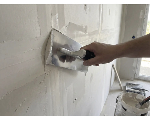 Artisan lisse un mur avec une lisseuse et du plâtre