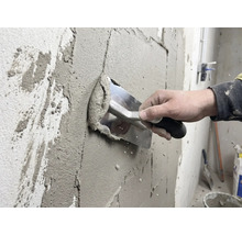 Handwerker trägt Putz mit einer Glättkelle auf eine Wand auf.