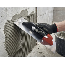 Application de colle à carrelage sur un mur à l'aide d'une truelle en acier inoxydable