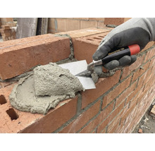 Maurerhand legt mit einer Maurerkelle Mörtel auf eine Ziegelsteinmauer.