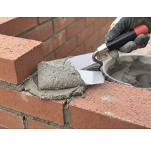 Un maçon travaille la brique avec une truelle et du mortier.