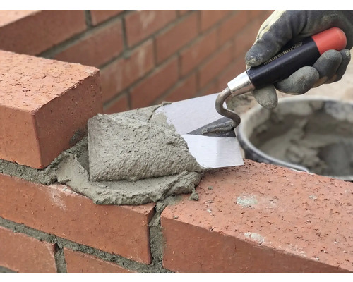 Un maçon travaille la brique avec une truelle et du mortier.